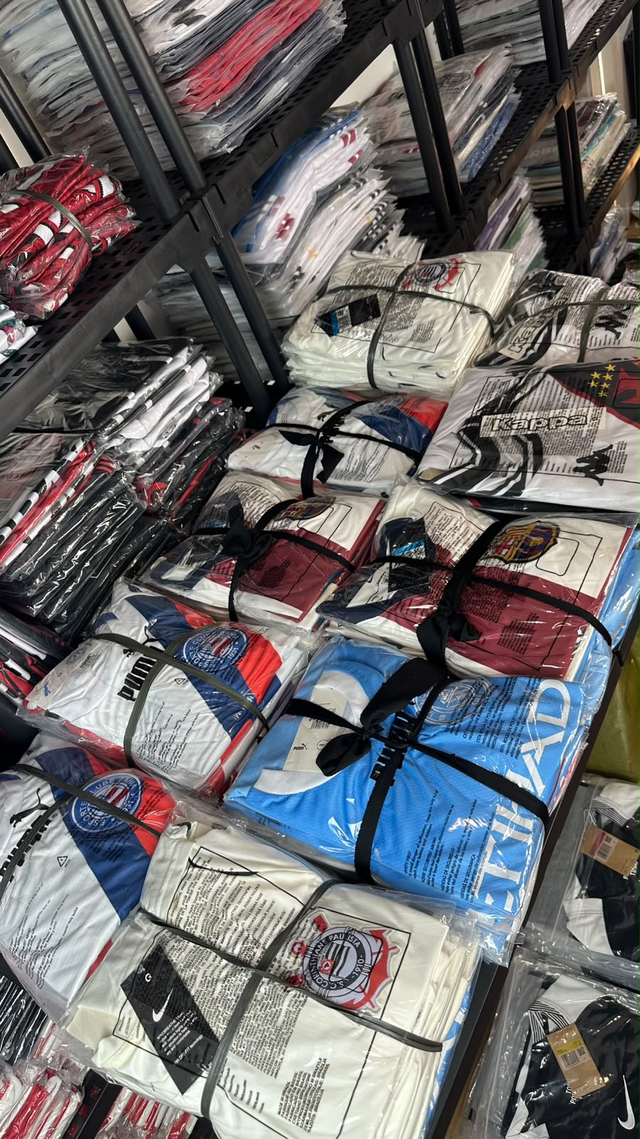 Prateleiras reais do estoque com camisas de time separadas por clube